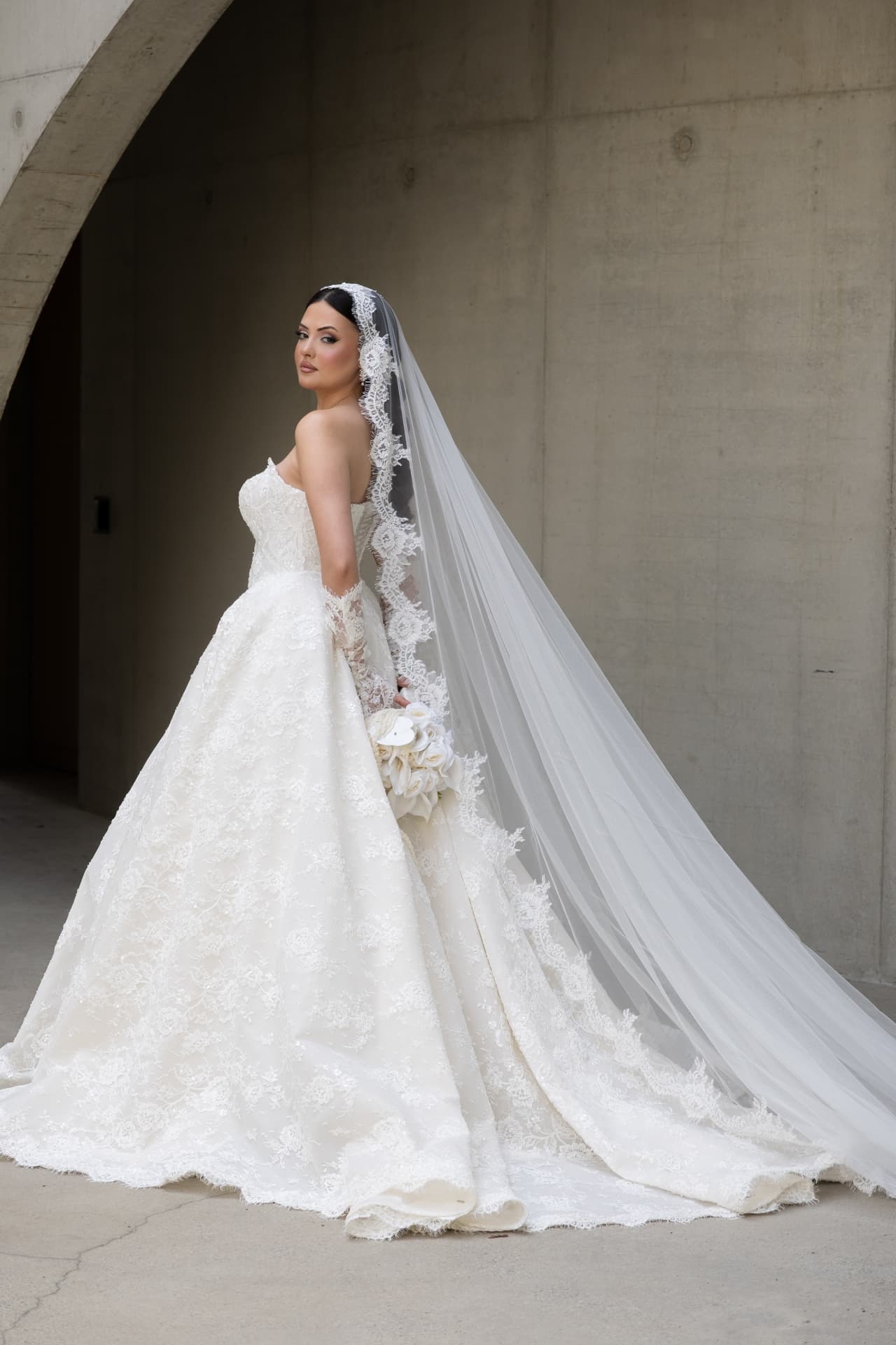 A bride with her lace wedding train against a concrete wall
