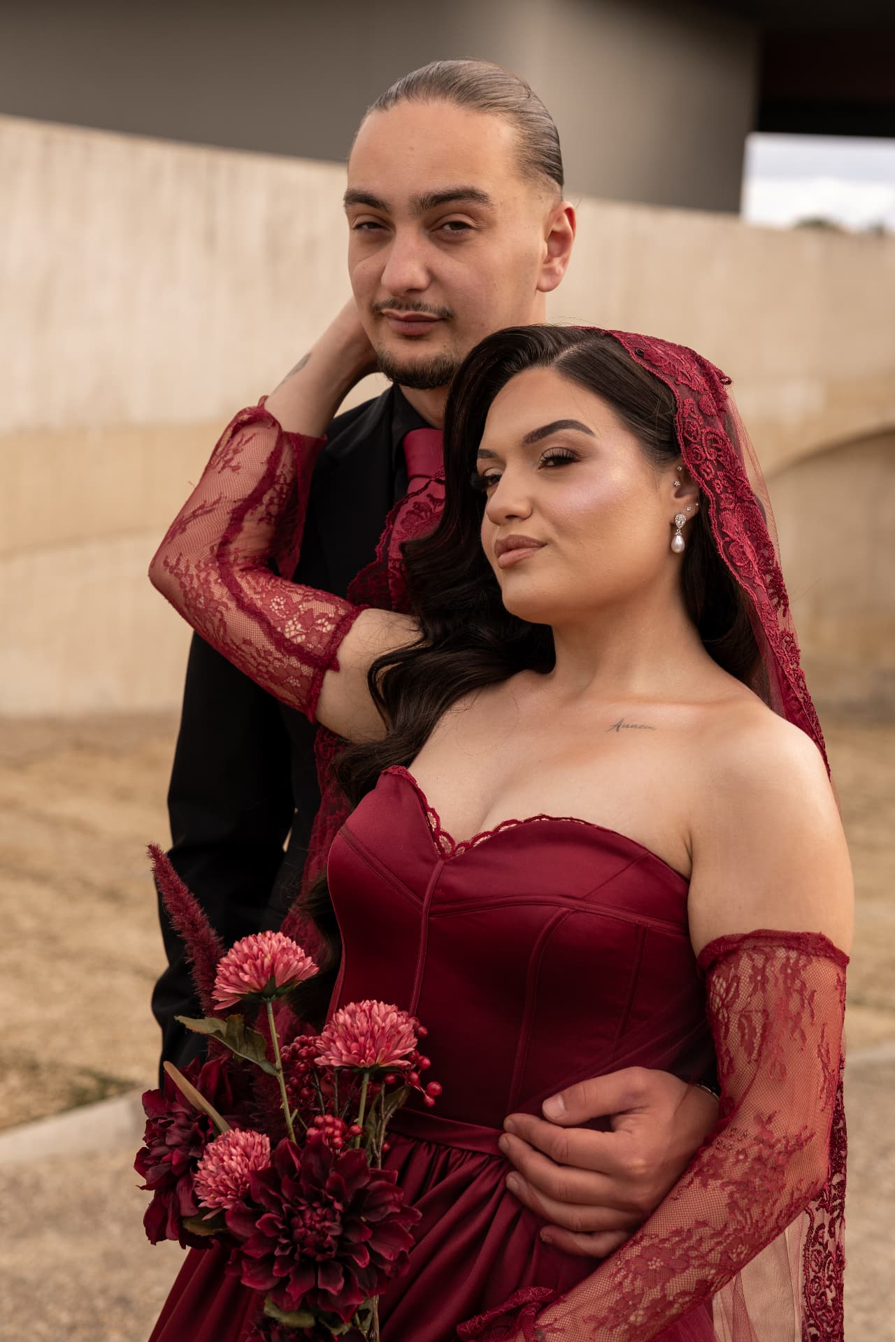 A burgundy bridal portrait with the groom beside a sunlit wall