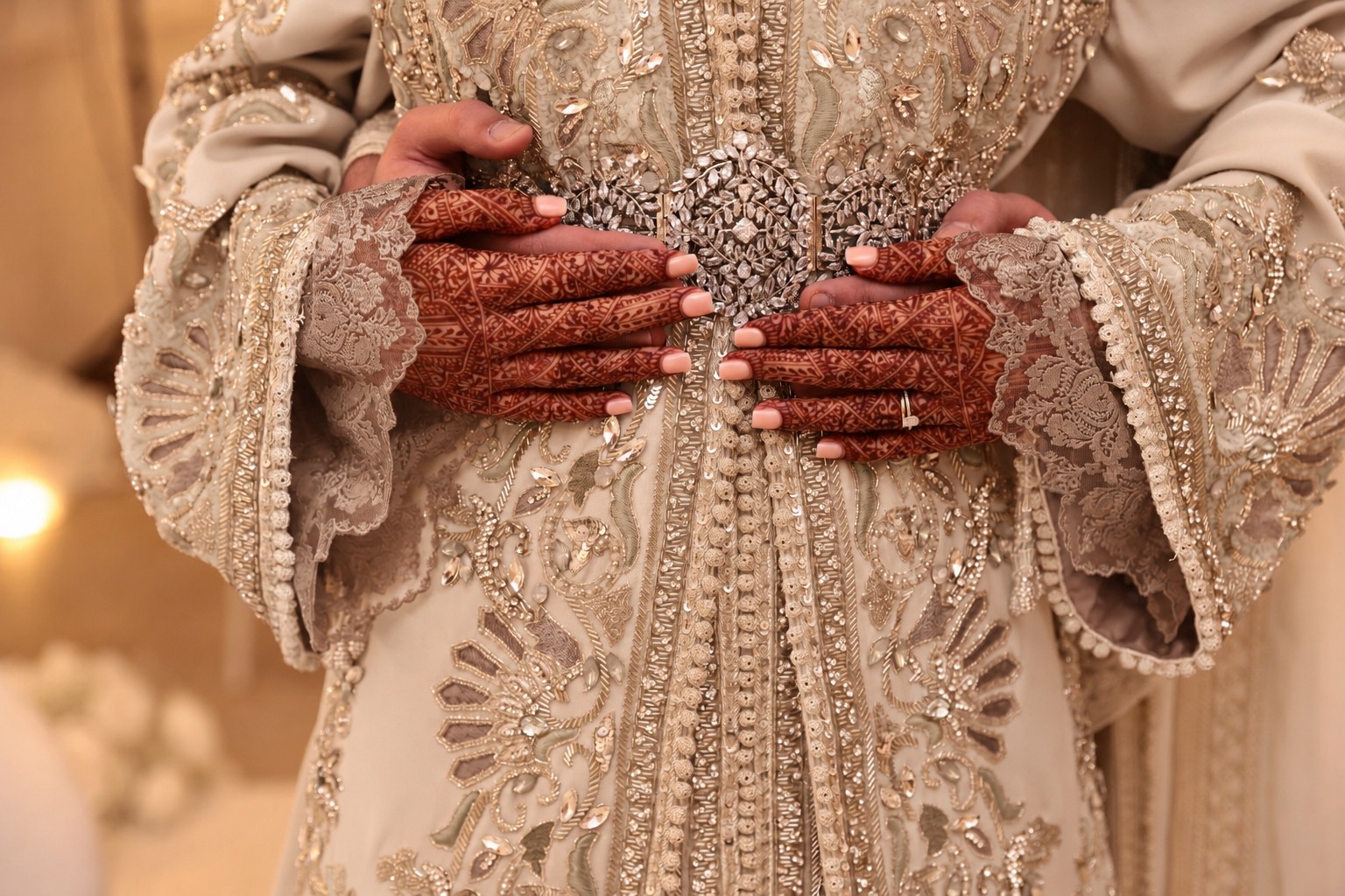 Henna-adorned hands resting on the beaded belt of a beige ceremonial gown