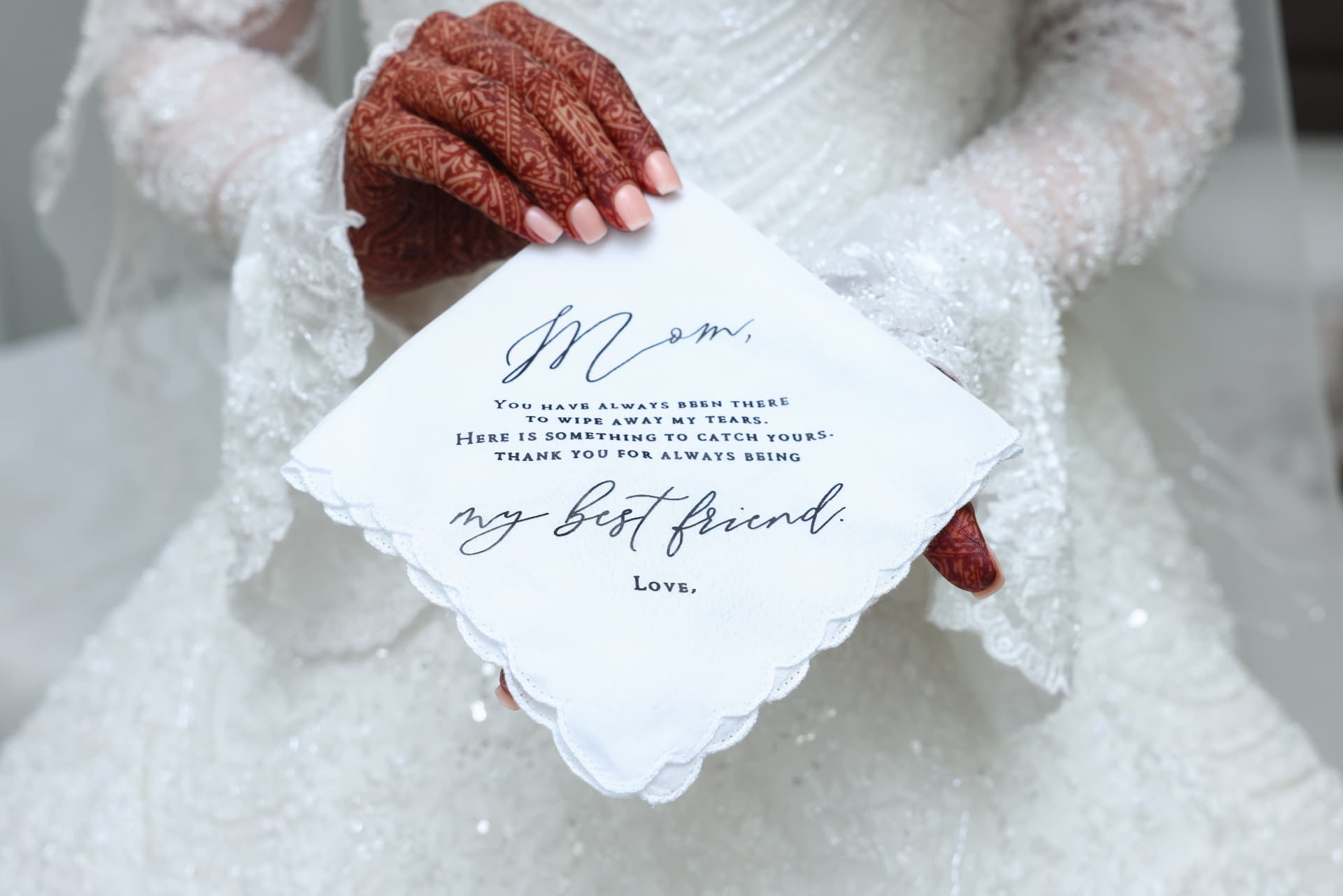 Henna-adorned hands holding a wedding invitation over a lace gown