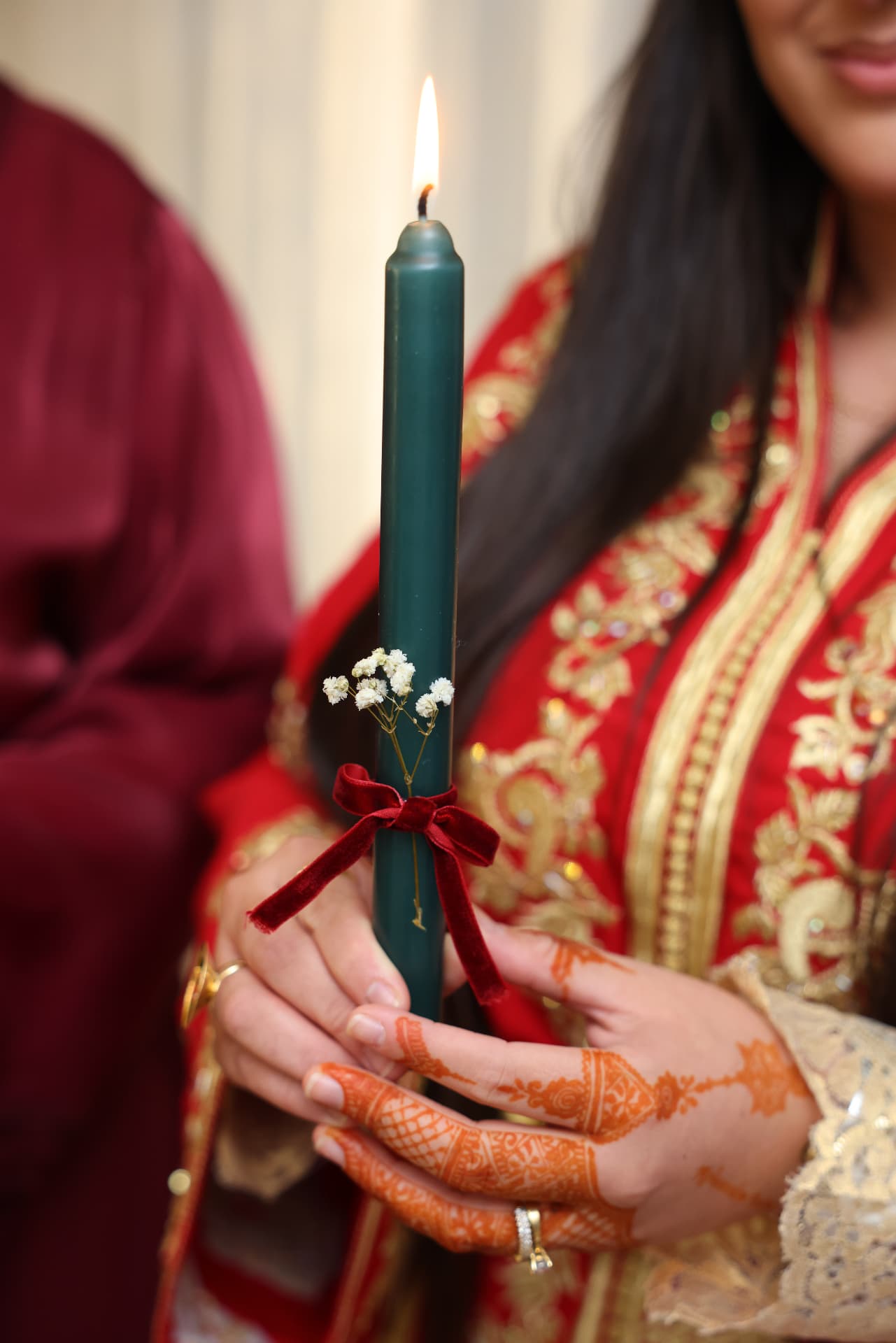 Hands holding a lit green candle beside red and gold embroidery