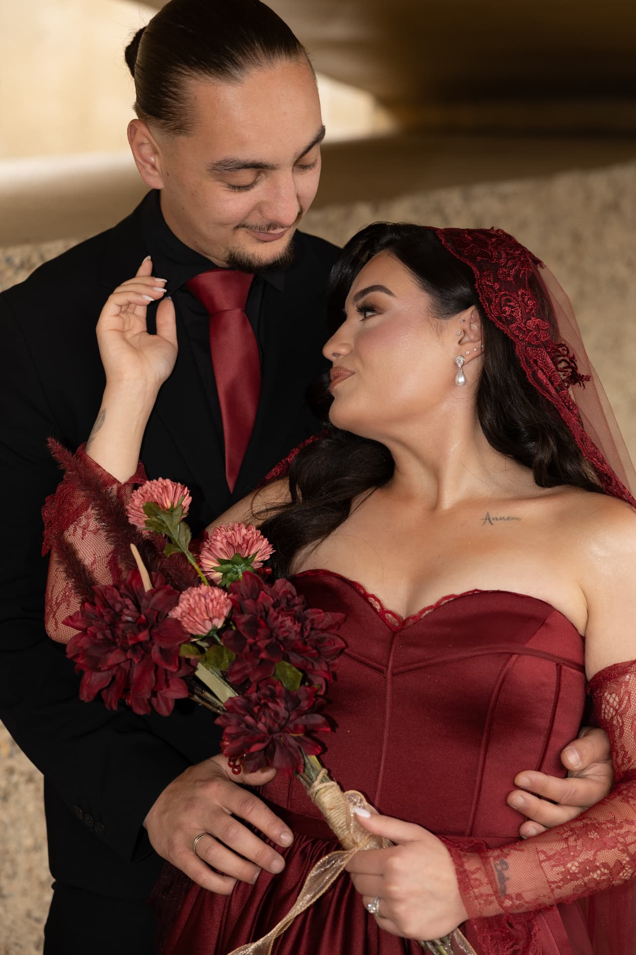 A couple sharing a tender glance with a deep red bridal bouquet