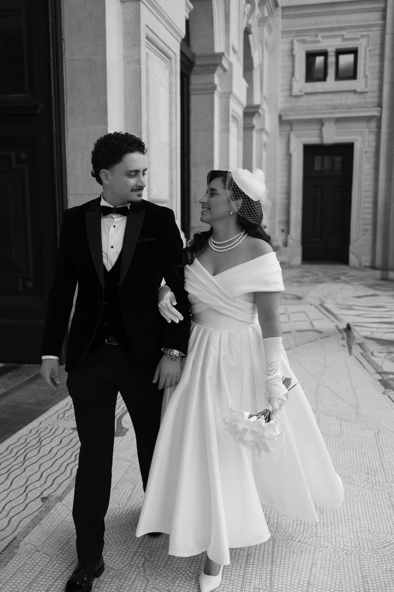 Black-and-white photograph of newlyweds walking beside an ornate building