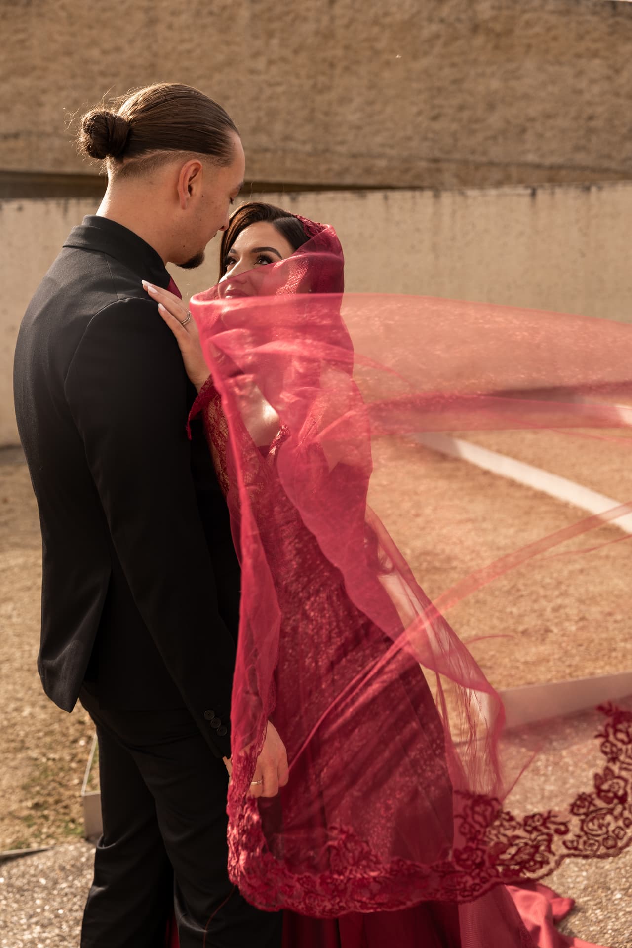 A bride and groom gazing at each other beneath a flowing red veil
