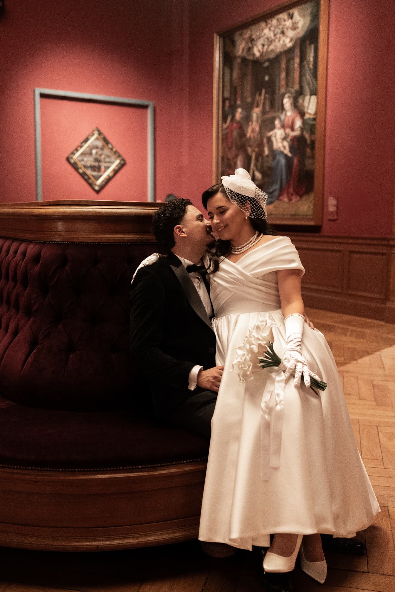 A bride and groom together on a curved seat in a red gallery room