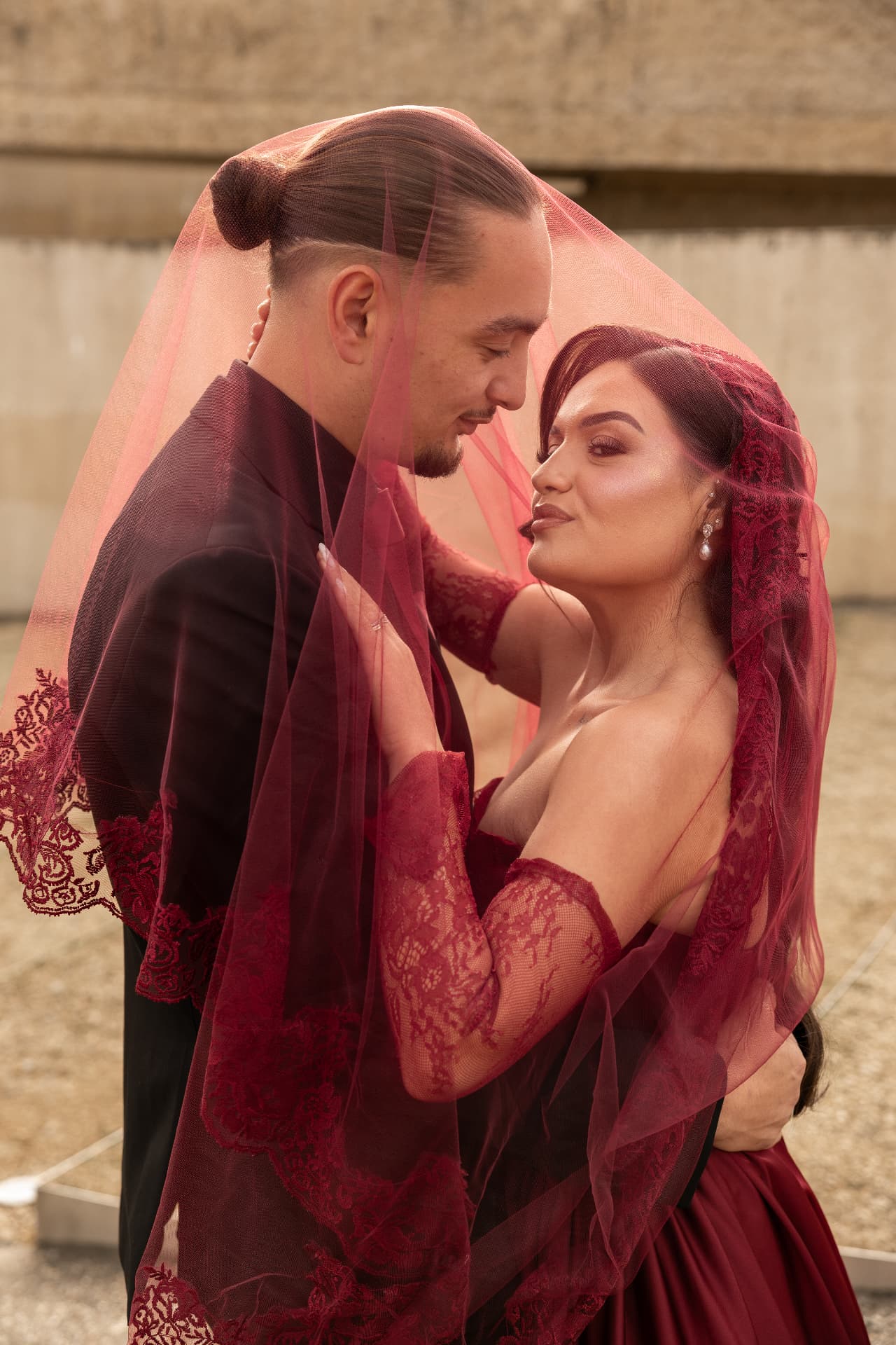 A close portrait of a couple wrapped in a red lace veil