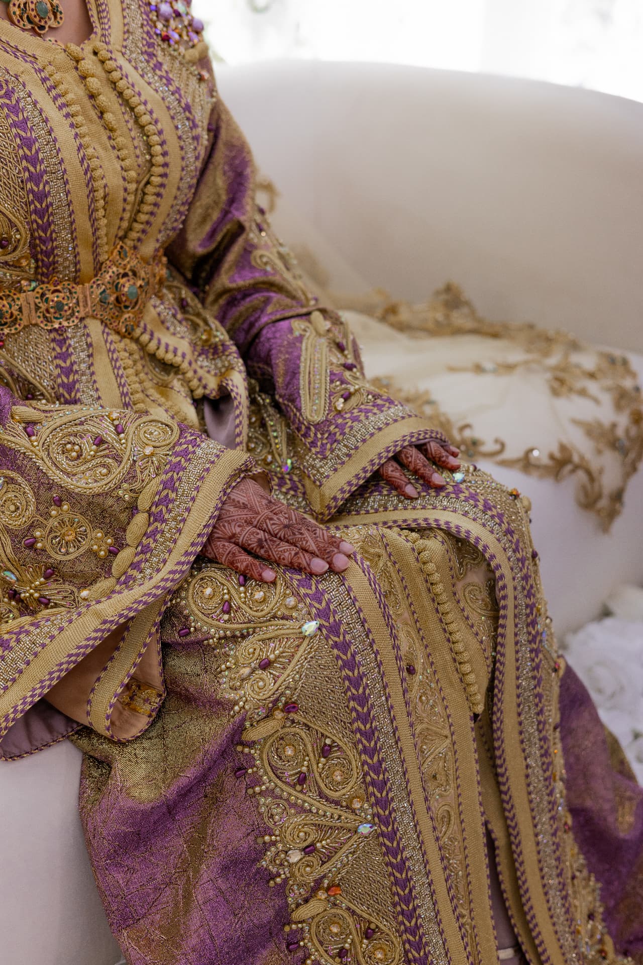 Henna-adorned hands resting on a purple and gold embroidered gown