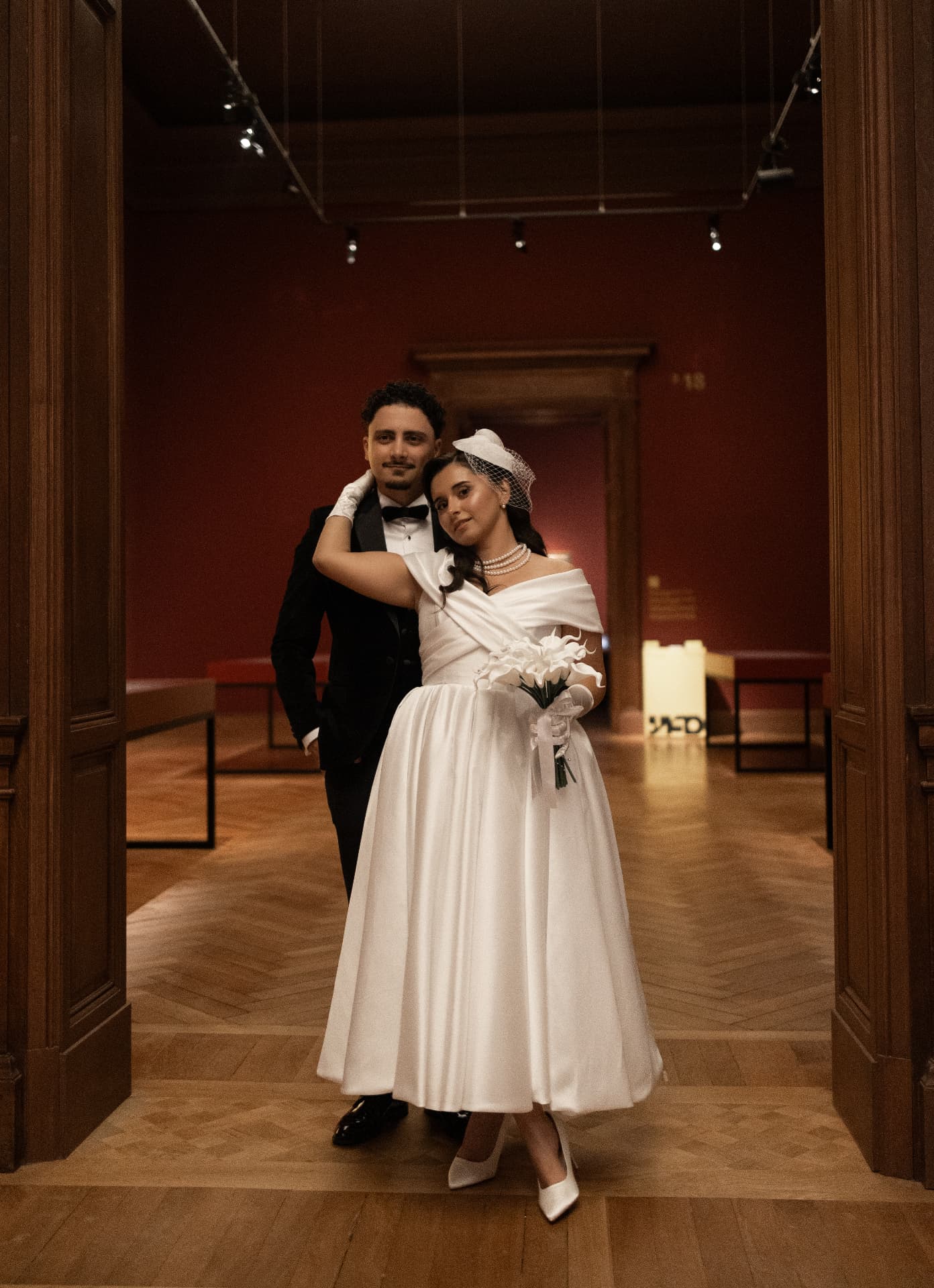 A full-length wedding portrait in a warmly lit gallery