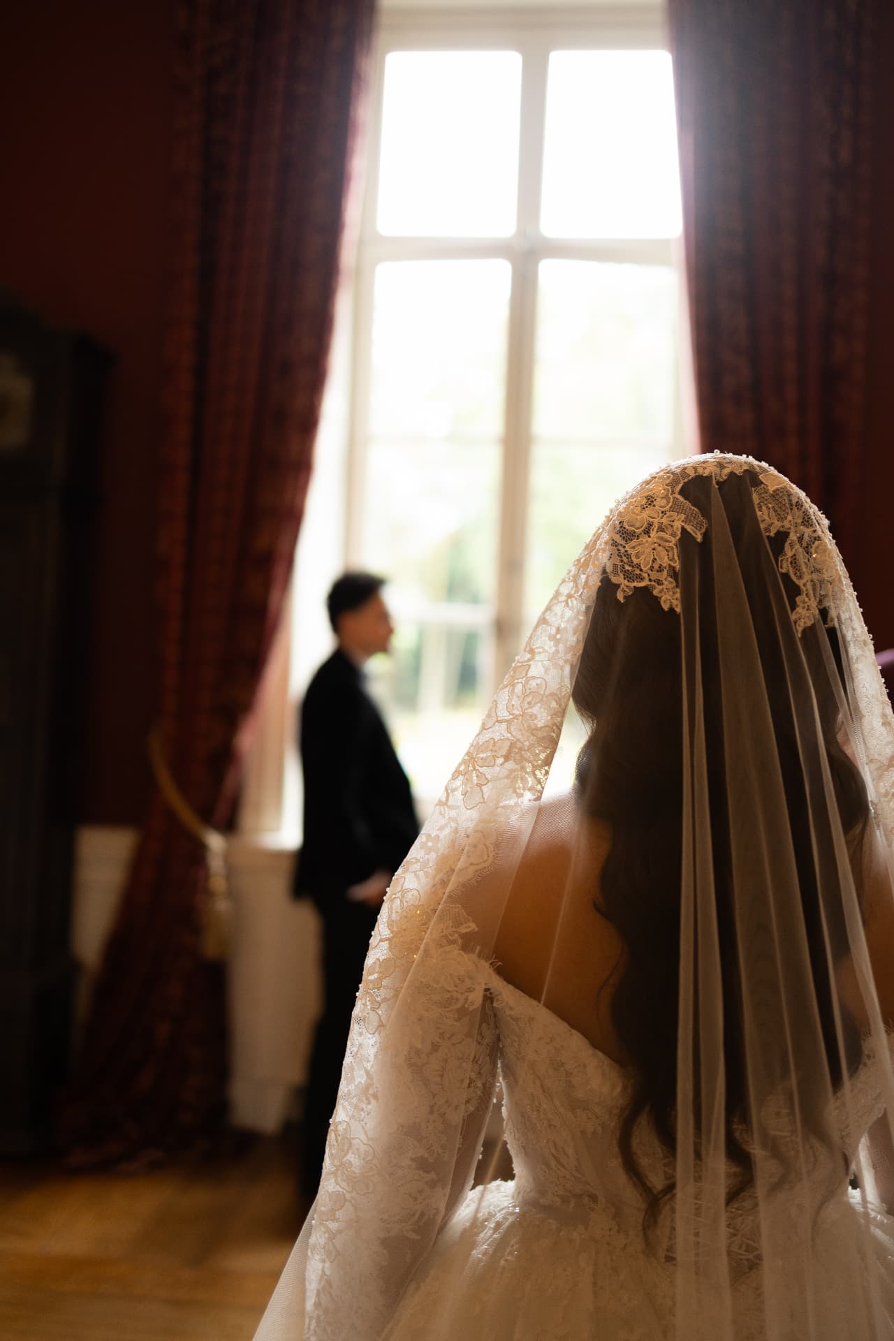 A bride's lace veil seen from behind beside a softly lit window