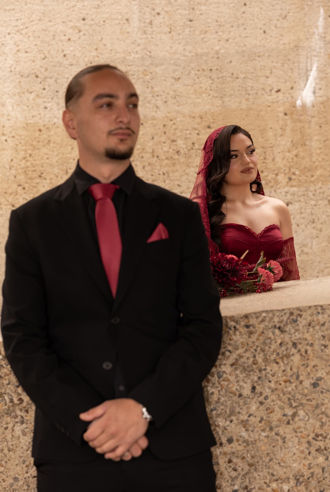 A couple in burgundy and black framed by a textured stone wall