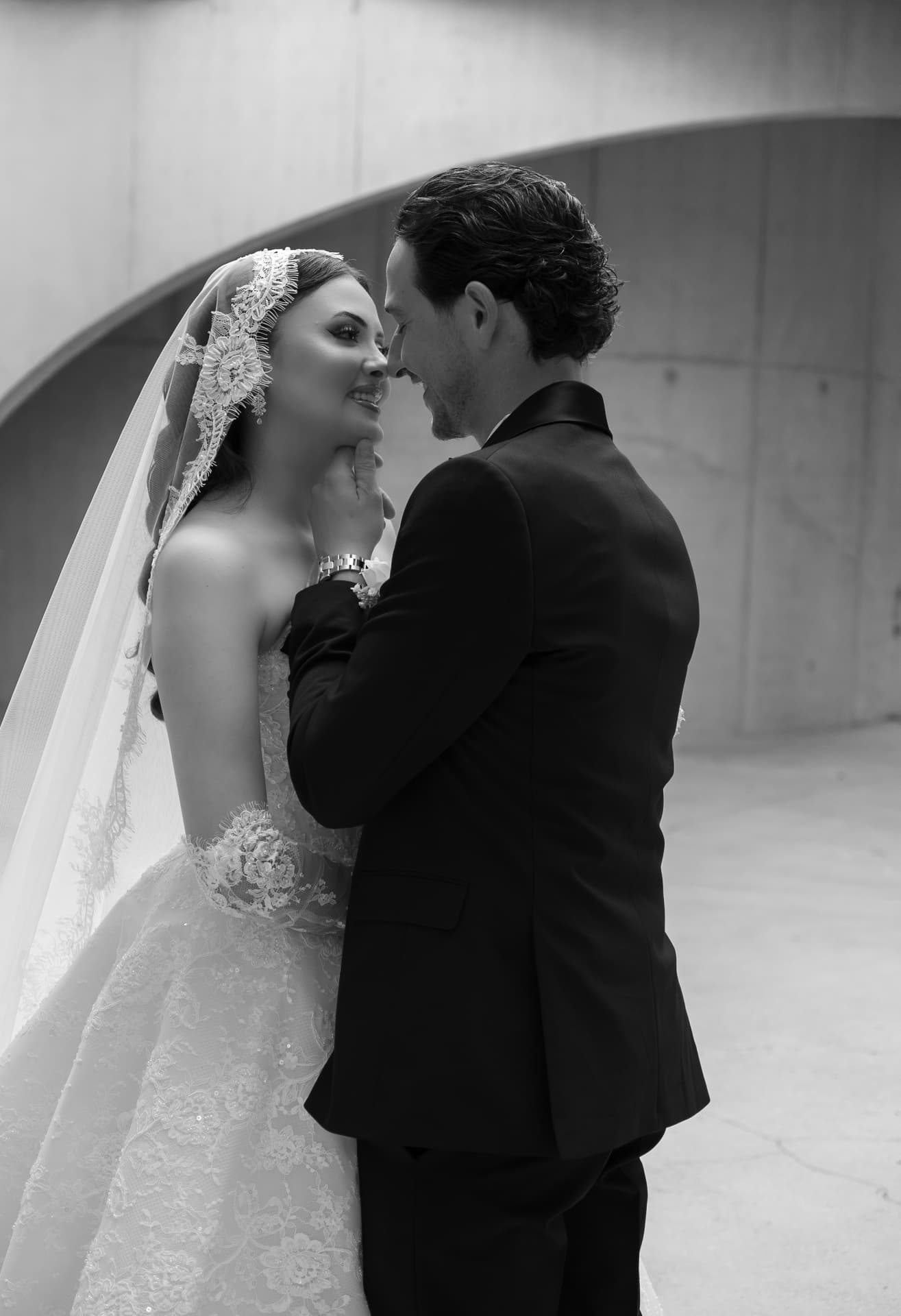 Black-and-white close wedding portrait beneath a concrete archway