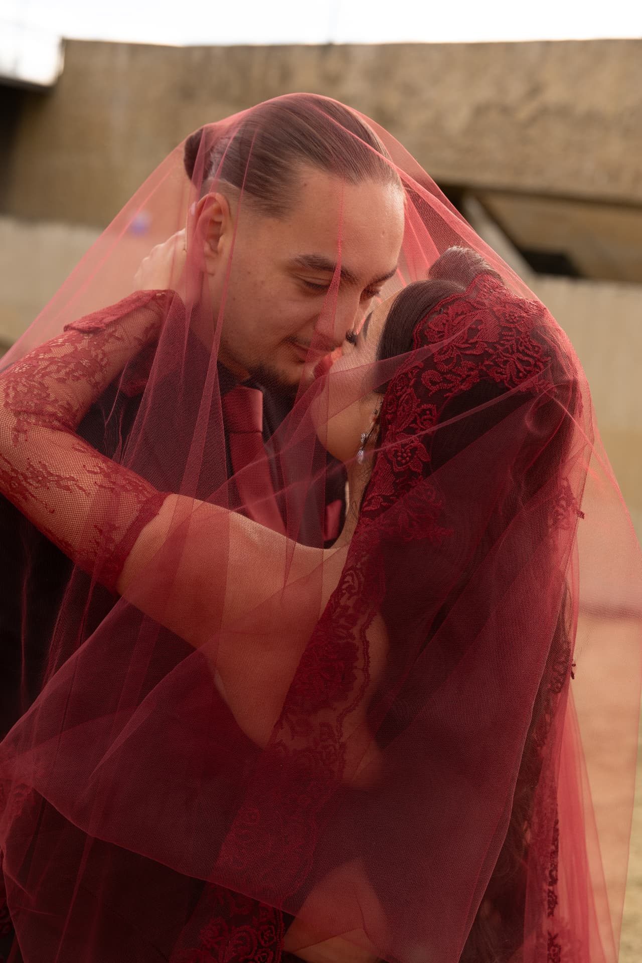 A couple sharing a kiss beneath a translucent red veil