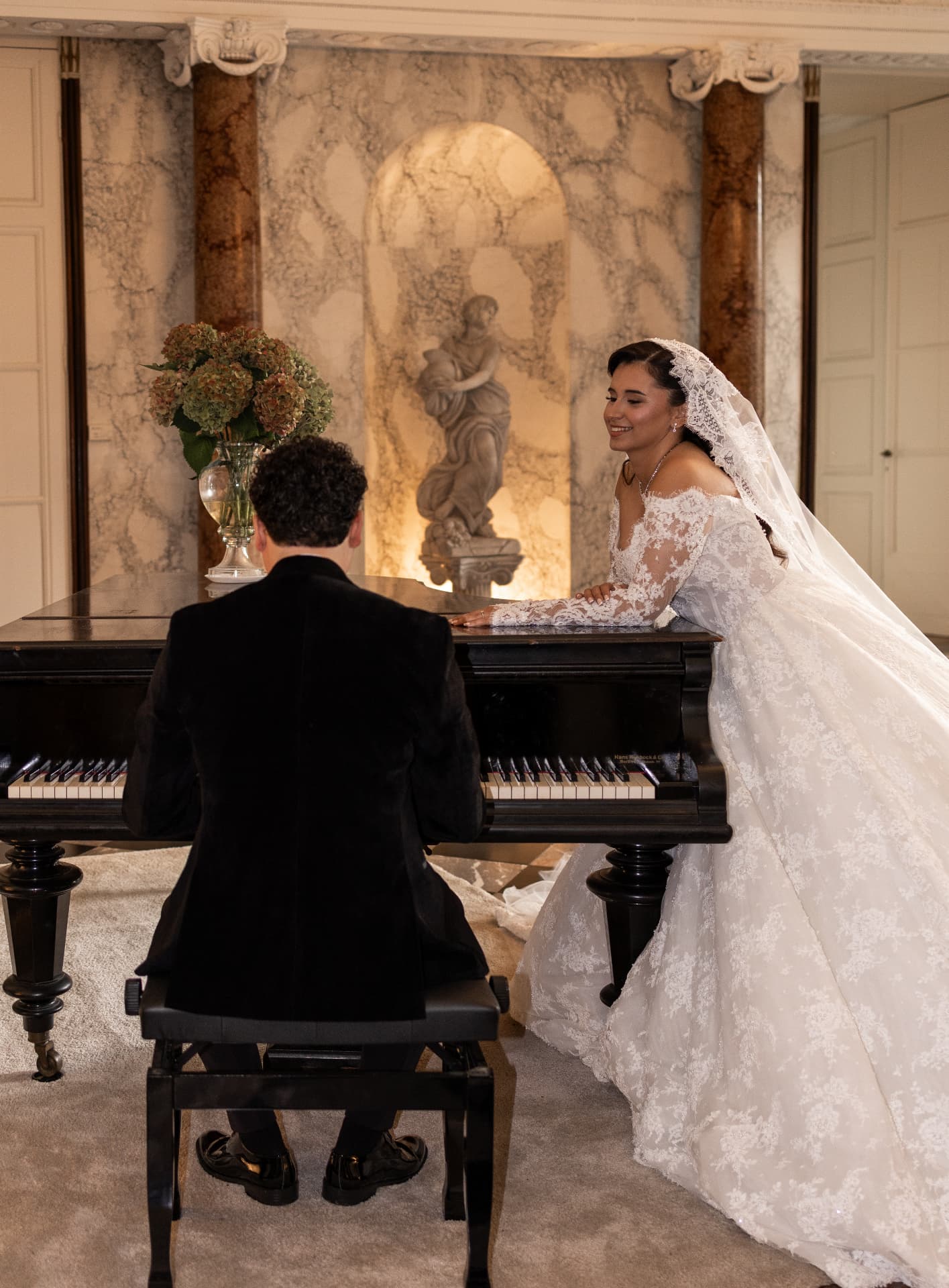 A groom seated at a piano beside his bride in an ornate interior
